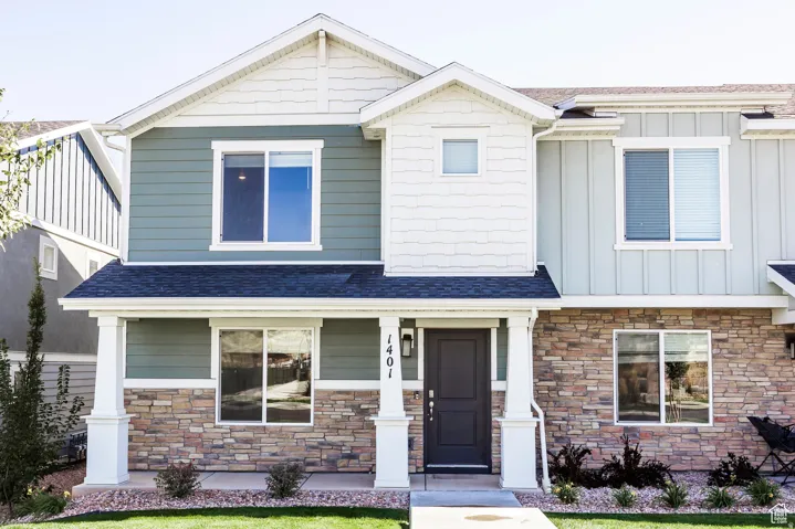 Front exterior showcasing a stone facade, muted green siding, white trim, a dark entry door, and a covered porch with white columns
