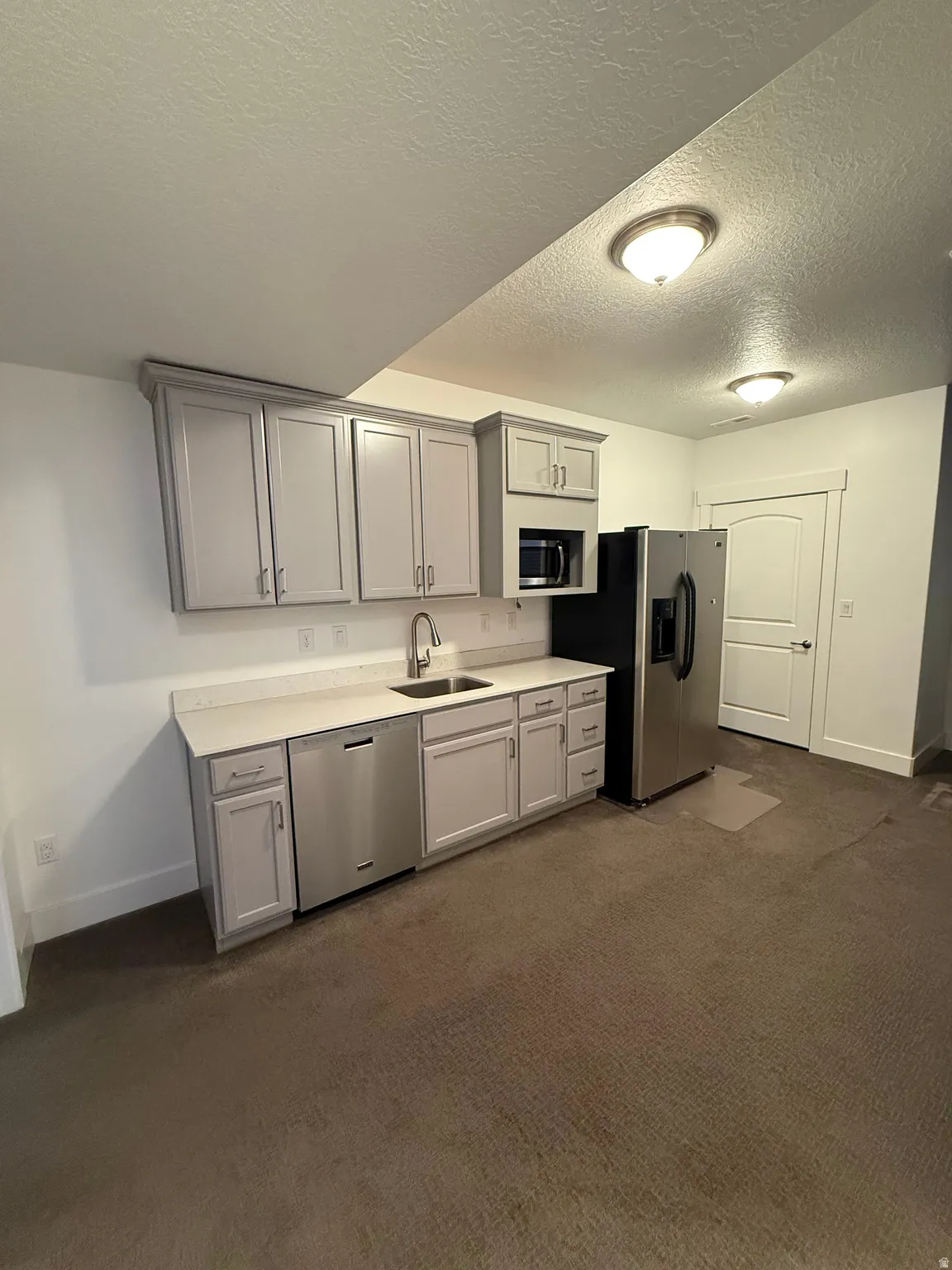 Compact kitchen area featuring gray cabinetry, stainless steel appliances, a white solid surface countertop, and an undermount sink with a gooseneck faucet