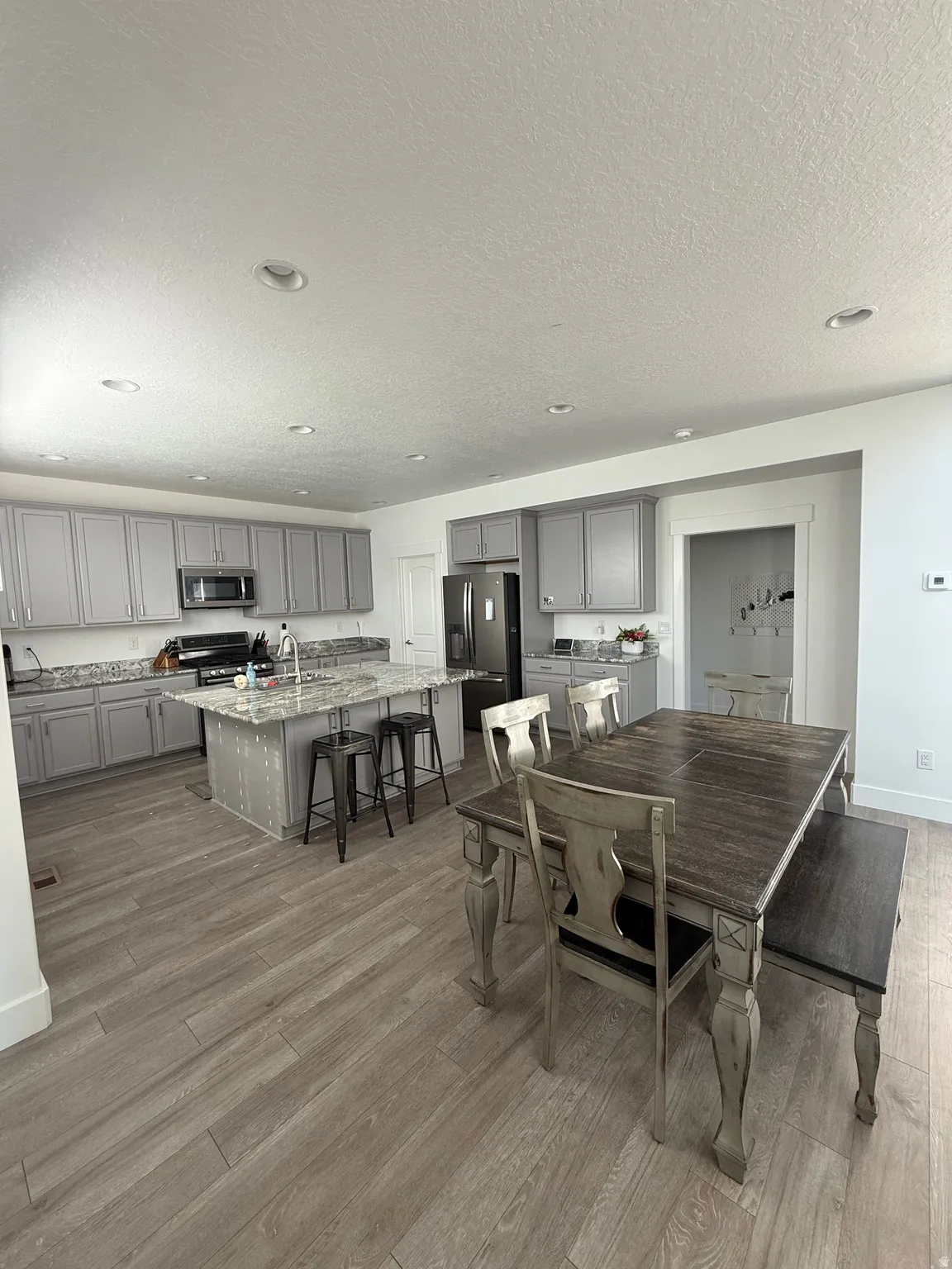 Open-concept kitchen and dining area featuring wood-finish flooring, recessed lighting, gray cabinetry, and a central kitchen island with seating