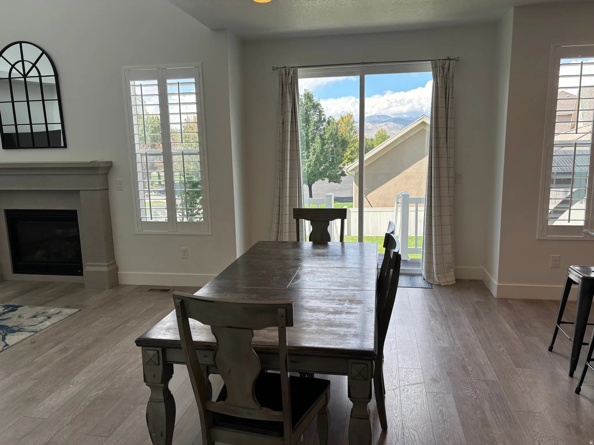 Hardwood-style flooring throughout, featuring a fireplace with a mantel, a sliding glass door, and plantation shutters