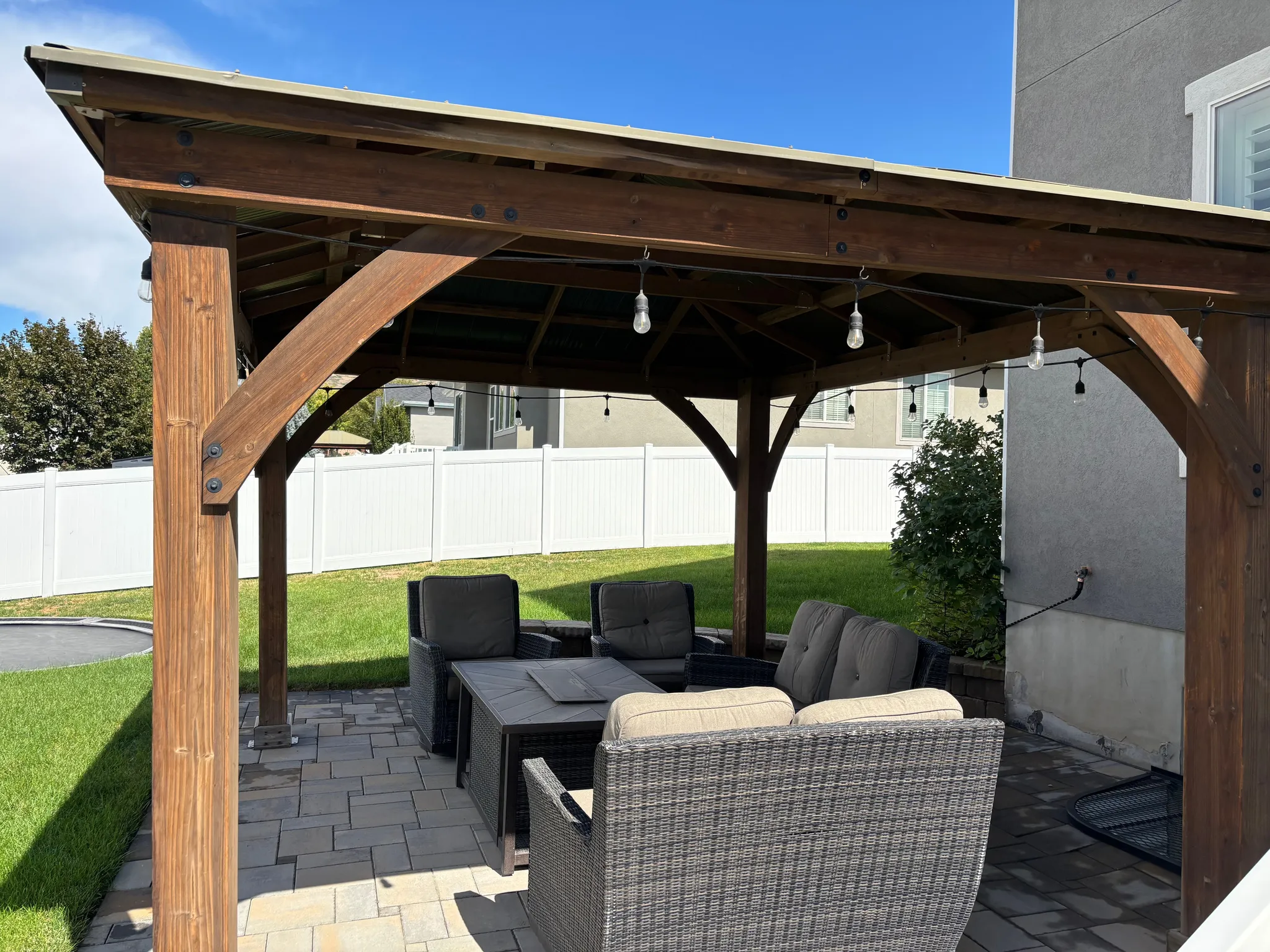Patio area featuring a wood-beam pergola with string lighting, paver flooring, and a surrounding privacy fence