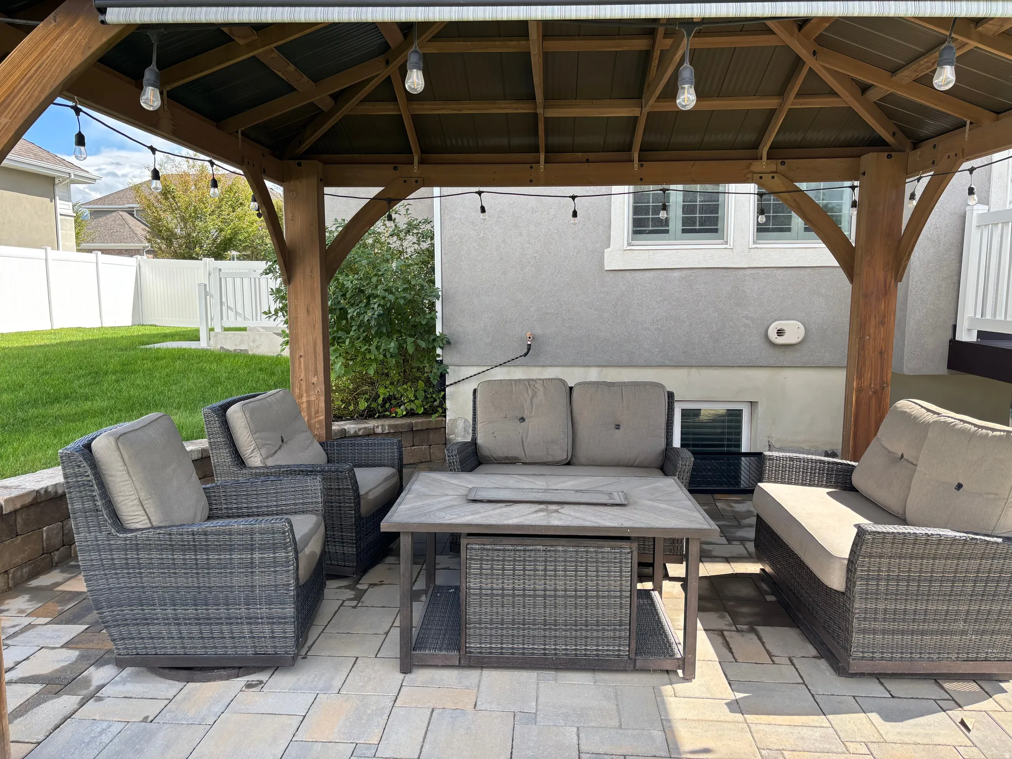 Paver patio featuring a wooden gazebo with string lighting, stone retaining wall, and a privacy fence