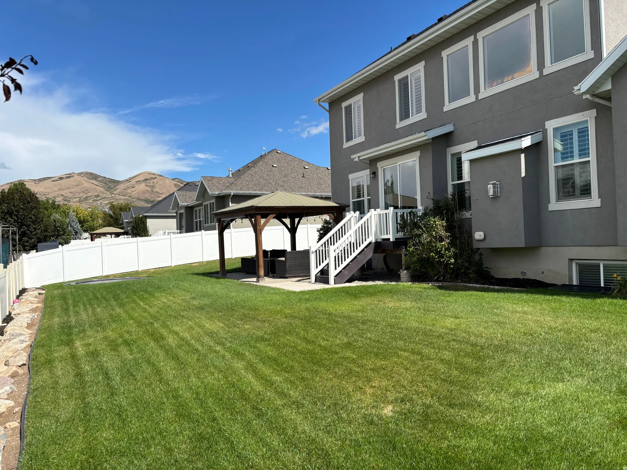 Expansive lawn area, stucco exterior, rear deck with white railings, sliding glass door, and a built-in gazebo