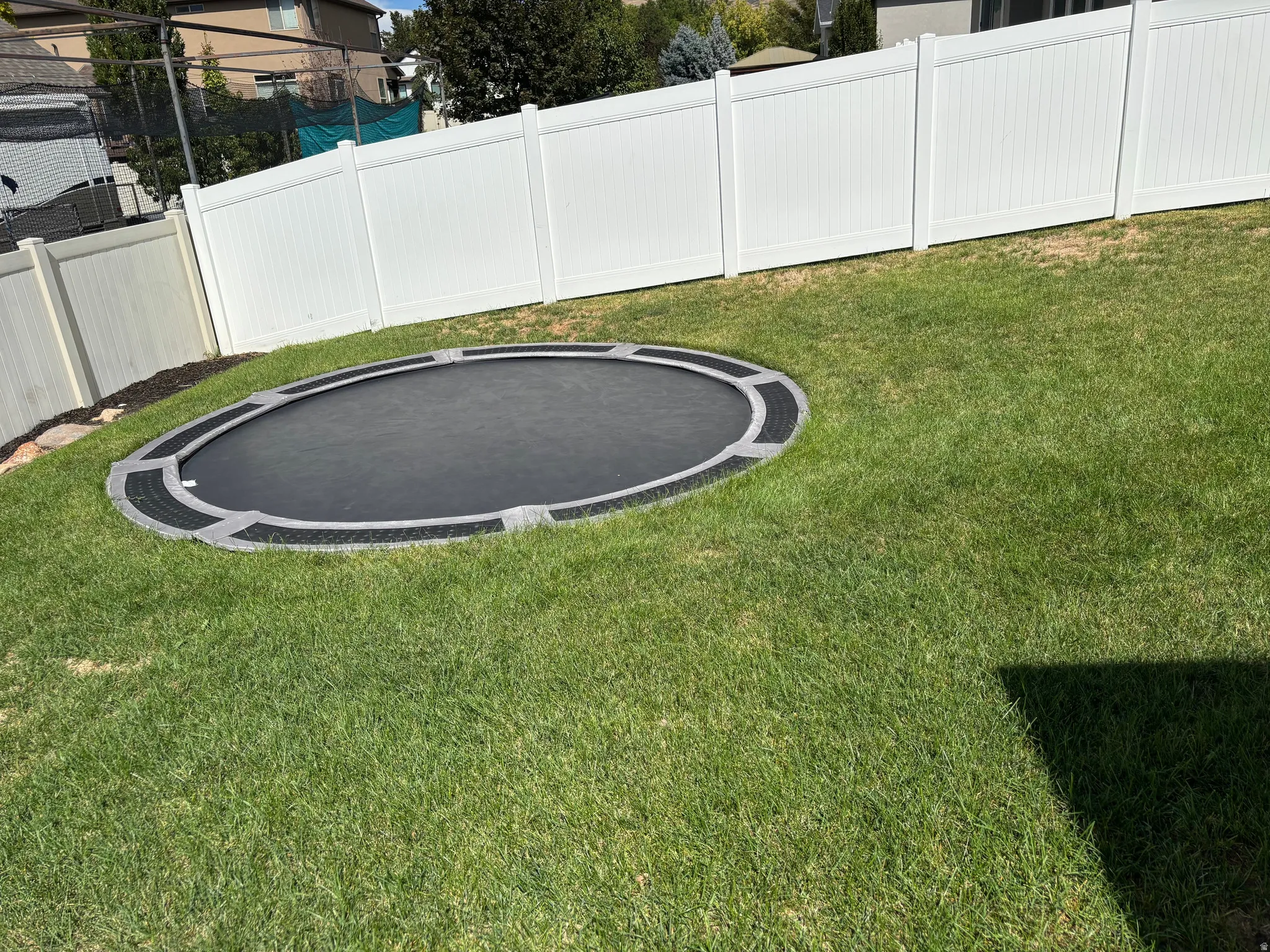 Grassed outdoor area with a white privacy fence and an in-ground round trampoline
