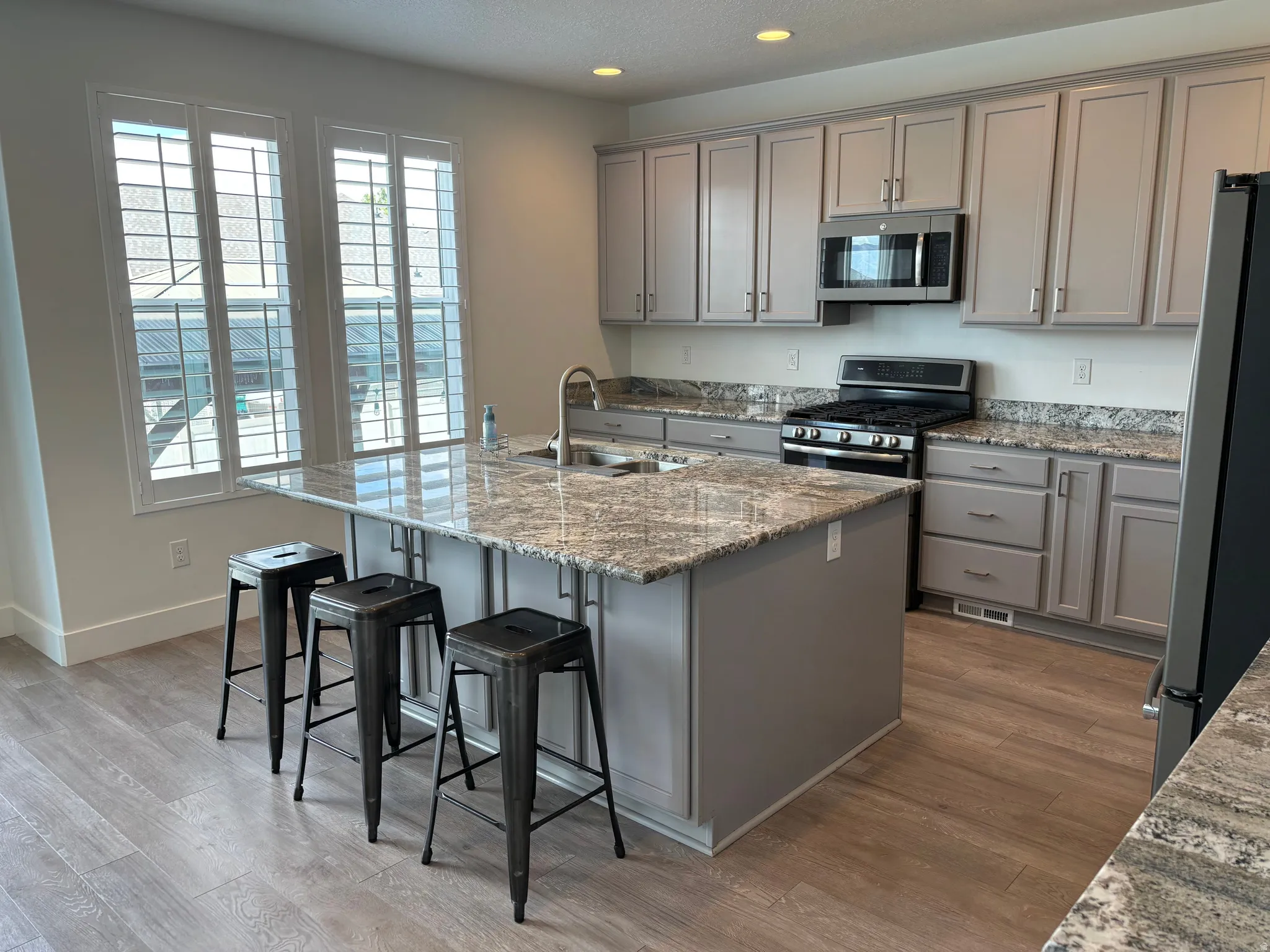 Kitchen featuring a large island with sink, stainless steel appliances, wood-finish flooring, light grey cabinetry, and stone countertops