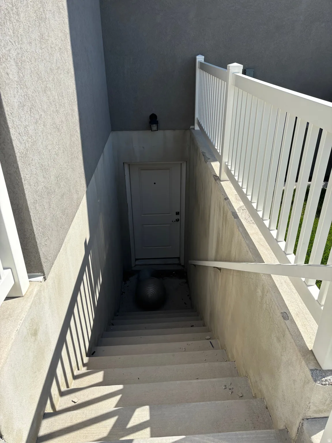 Concrete basement access with a white entry door, concrete steps, and a white railing