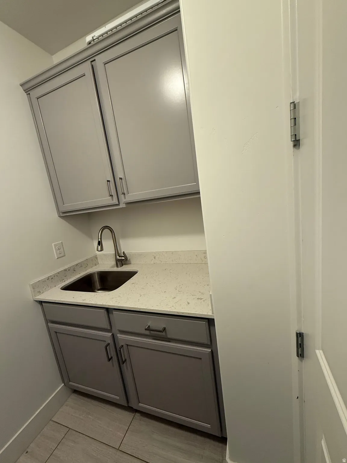 Utility sink with brushed nickel faucet, light gray cabinetry, and a speckled countertop