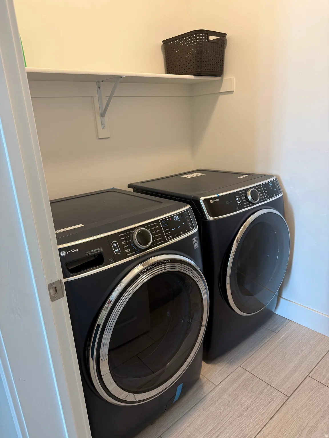 Laundry area featuring a built-in white shelf, light-toned wall paint, and wood-finish tile flooring