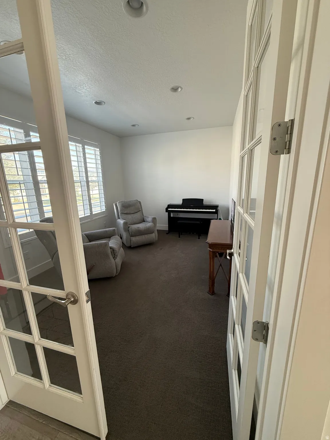 French doors opening into a carpeted room with multiple recessed lights and window shutters