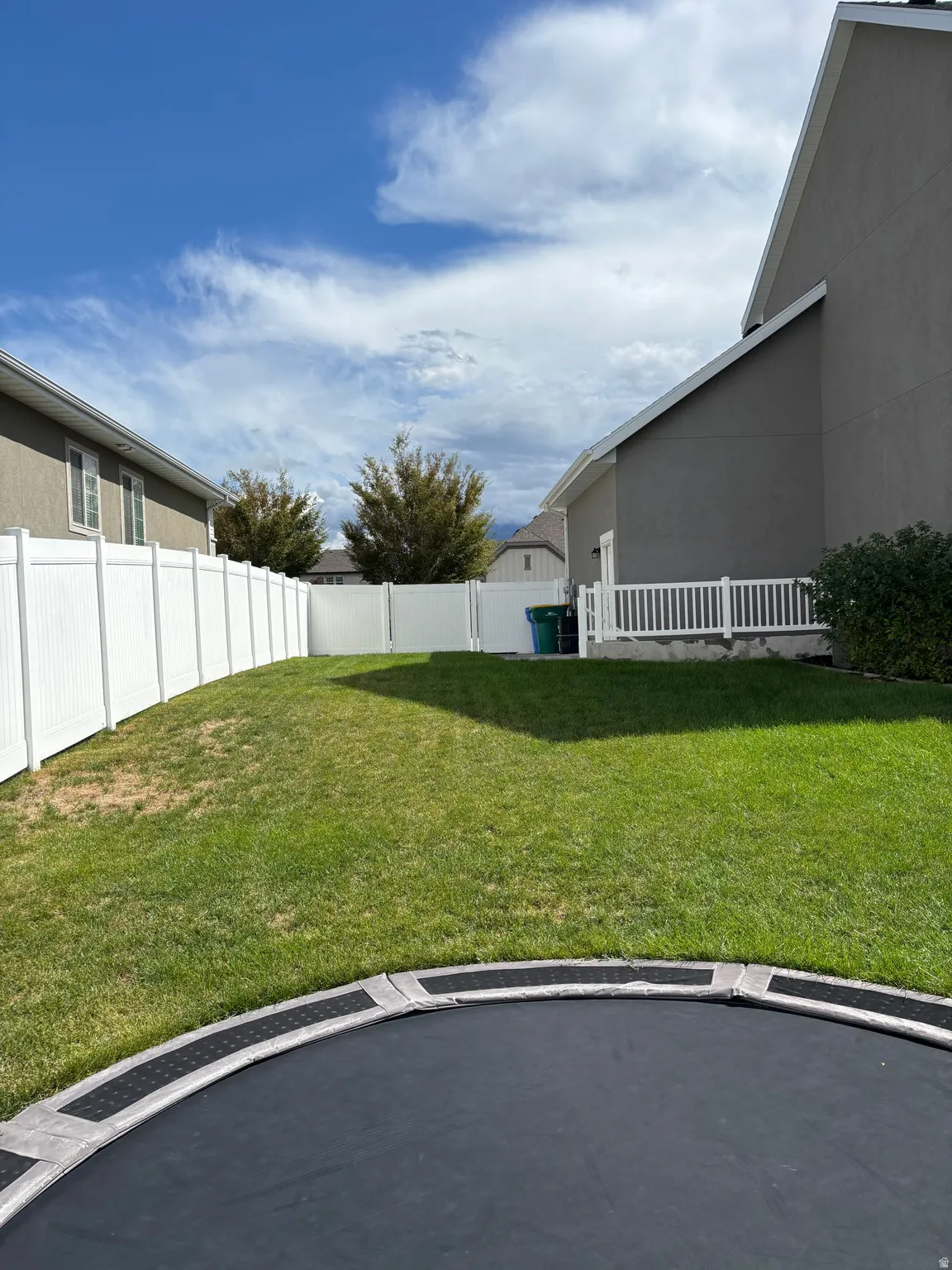 Expansive backyard featuring a green lawn, white vinyl fencing, and a white railing
