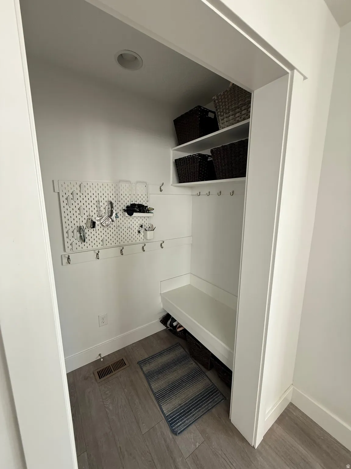 Recessed ceiling lighting illuminates a built-in bench, integrated shelving, and wall-mounted hooks