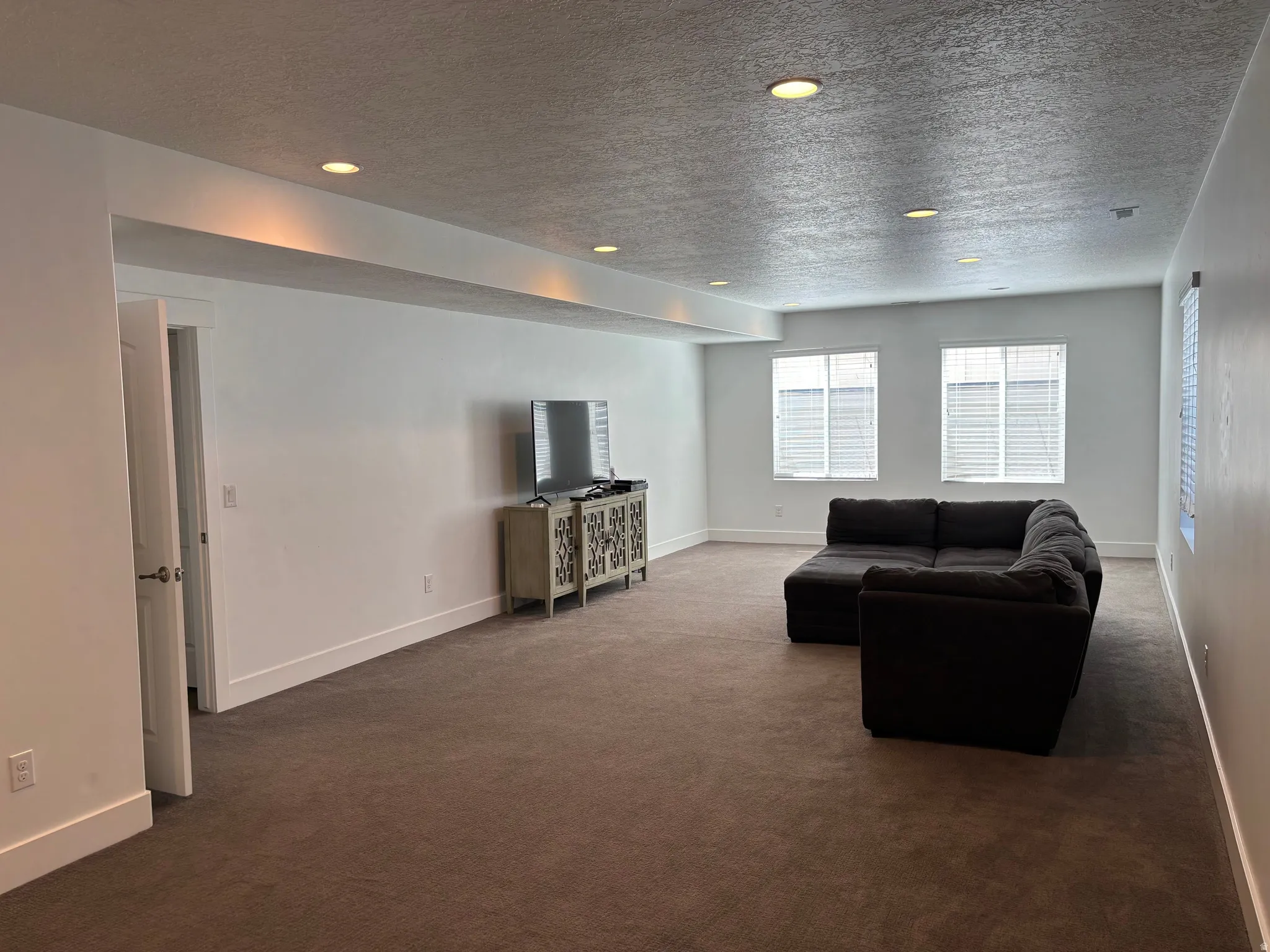 Spacious room featuring neutral carpeting, recessed lighting, and multiple windows with horizontal blinds