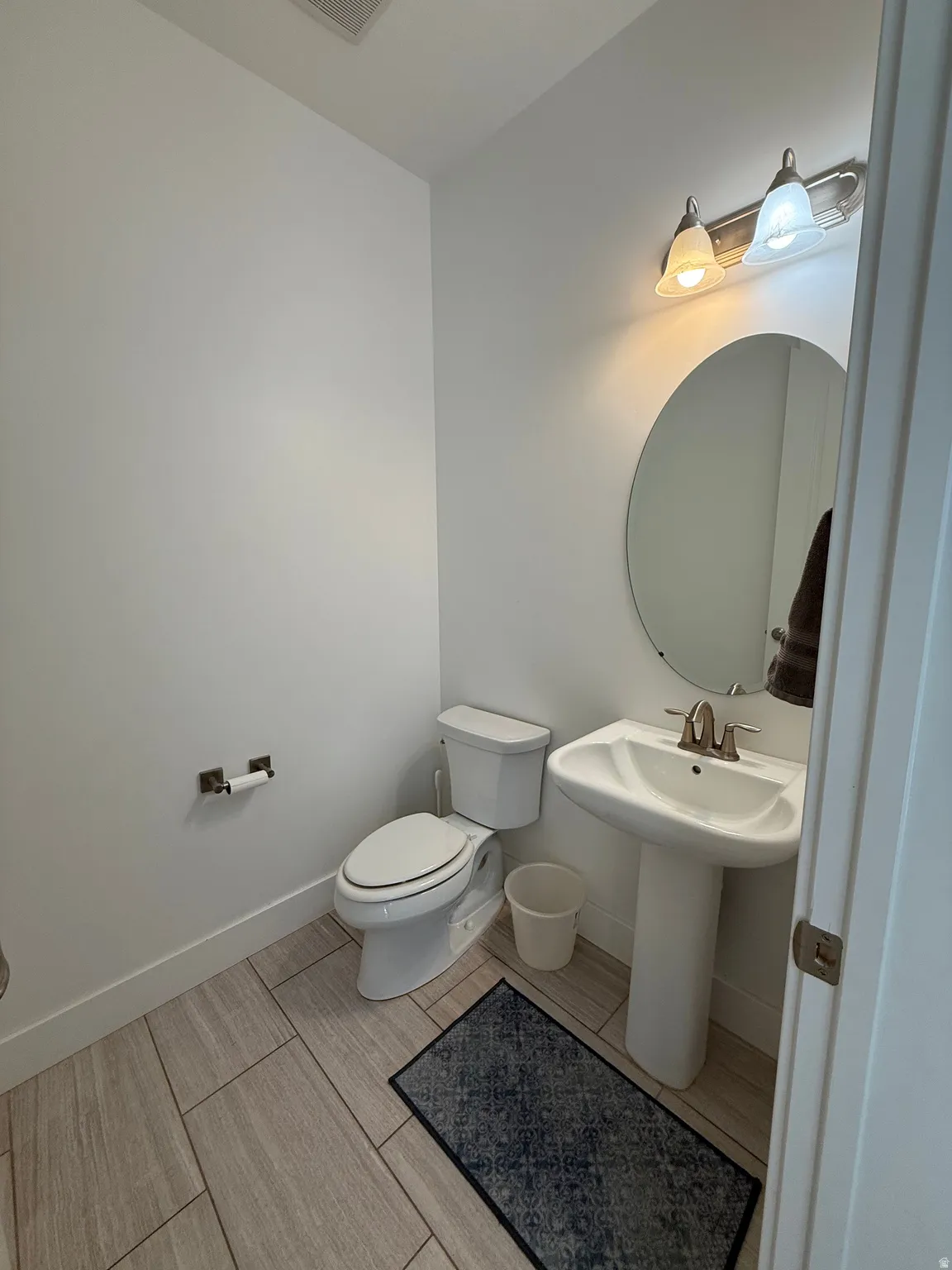 Powder room featuring a pedestal sink with a brushed nickel faucet, a rounded mirror, and a two-light vanity fixture