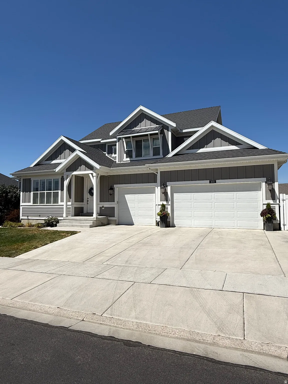 Craftsman-style exterior featuring gray horizontal siding, white trim, a dark gray shingle roof, a three-car garage, and a concrete driveway