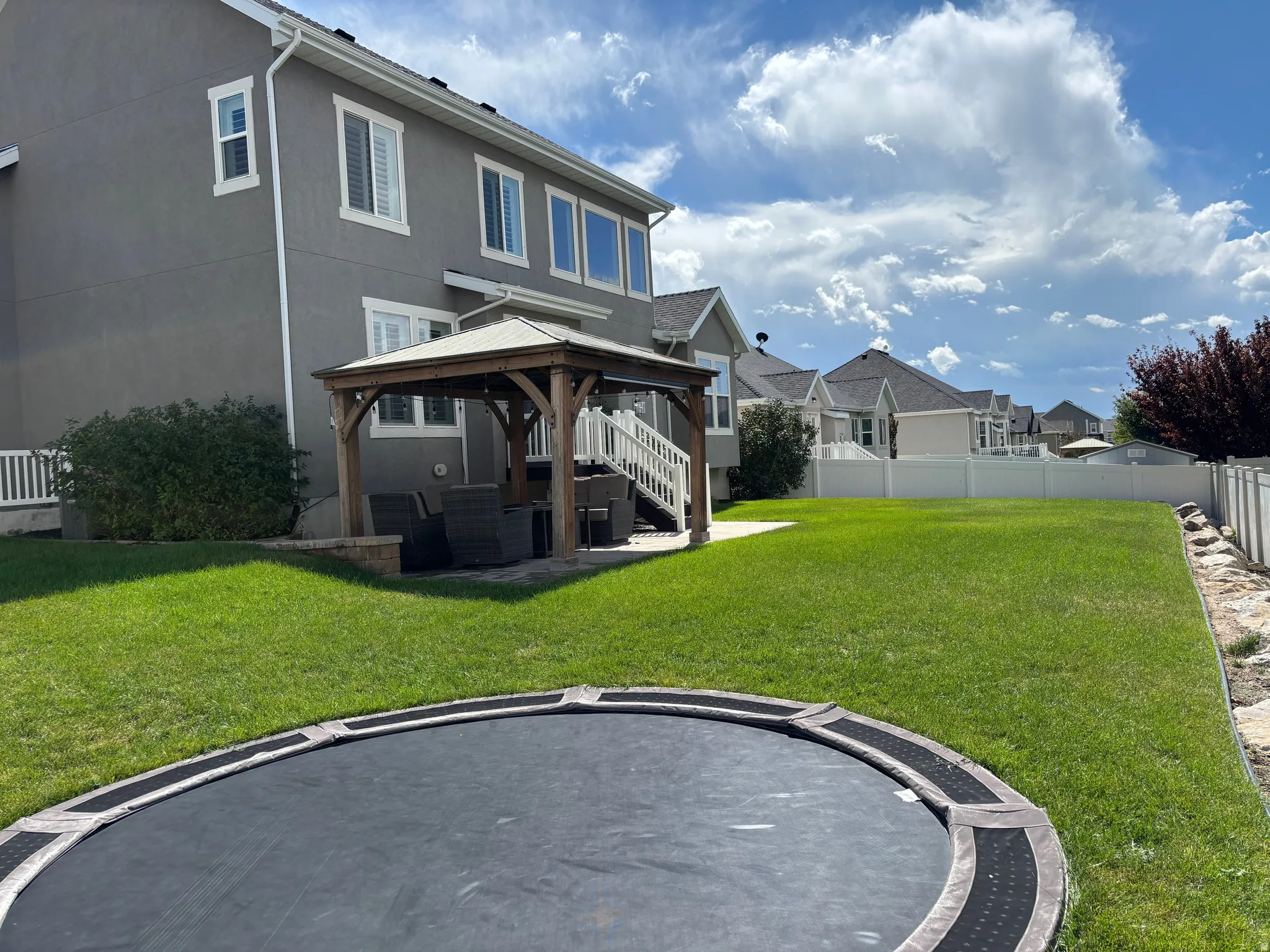 Expansive grassy yard with a gazebo, patio, and white privacy fence