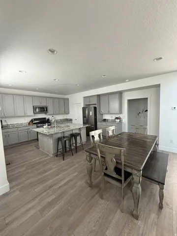 Open-concept kitchen and dining area featuring wood-finish flooring, recessed lighting, gray cabinetry, and a central kitchen island with seating