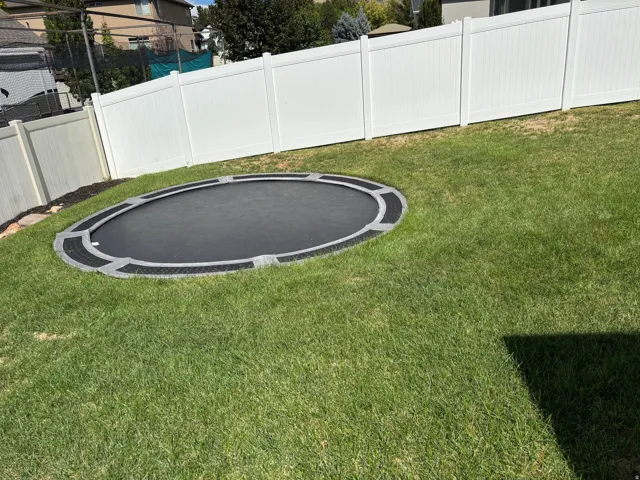 Grassed outdoor area with a white privacy fence and an in-ground round trampoline