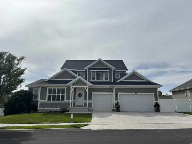 Gray siding exterior with white trim, covered front entry, attached three-car garage, and a concrete driveway