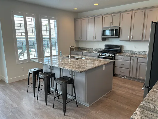 Kitchen featuring a large island with sink, stainless steel appliances, wood-finish flooring, light grey cabinetry, and stone countertops