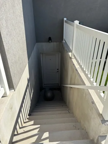 Concrete basement access with a white entry door, concrete steps, and a white railing
