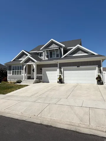 Craftsman-style exterior featuring gray horizontal siding, white trim, a dark gray shingle roof, a three-car garage, and a concrete driveway