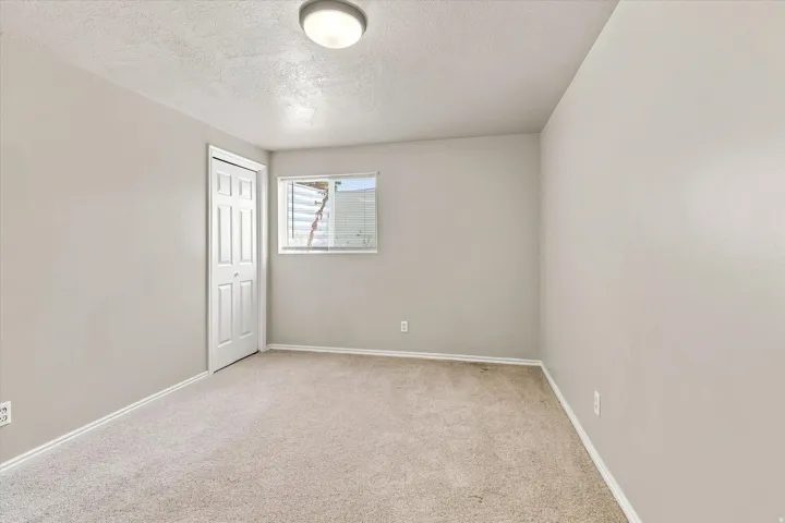Neutral-toned room featuring light-colored carpeting, a multi-pane window, and a white paneled bifold door