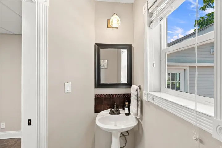 Pedestal sink with dark tile backsplash and a framed mirror