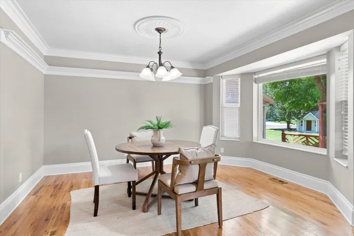 Dining area featuring wood-finish flooring, a bay window with blinds, and white crown molding