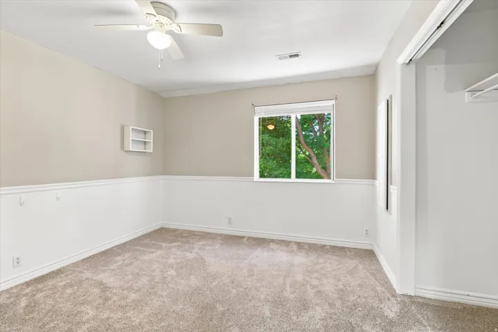 Carpeted room featuring a ceiling fan, crown molding, chair rail molding, and a built-in wall shelf