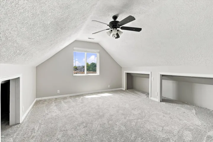 Spacious room featuring sloped ceilings, light gray carpet, and a multi-light ceiling fan