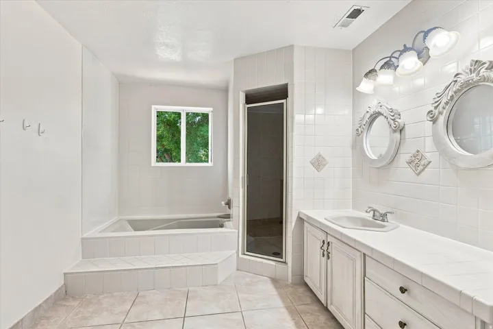 Bathroom featuring a built-in tub with tiled steps, a separate shower enclosure, and a double vanity with an integrated sink
