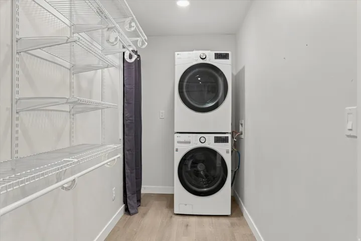 Laundry area featuring a stacked washer and dryer, wood-finish flooring, recessed lighting, and white wire shelving