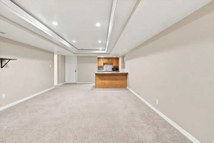 Recessed lighting illuminates this room, featuring light-toned carpeting and a partial built-in bar with wood-finish cabinetry and a stone-look countertop