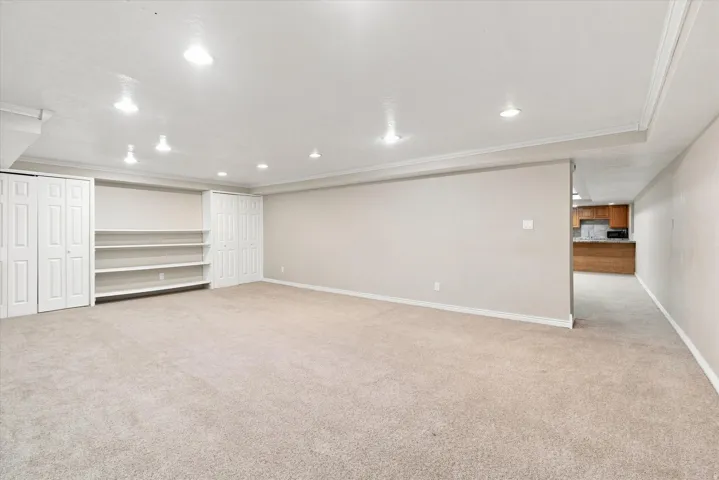 Spacious carpeted room featuring recessed lighting, crown molding, built-in shelving, and two sets of bi-fold closet doors