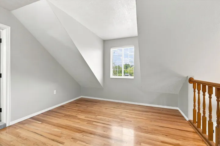 Upper level room featuring light wood-finish flooring, a window with horizontal blinds, and a wood spindle railing