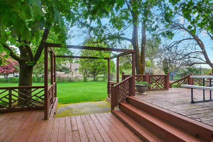 Spacious wood deck with railing and steps, featuring an open pergola structure and offering direct access to a large grass lawn