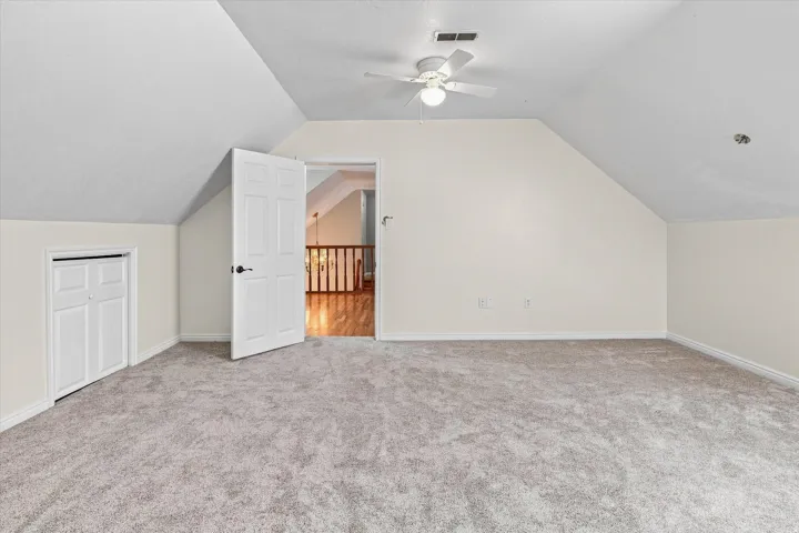 Spacious carpeted room featuring vaulted ceilings, a ceiling fan with integrated lighting, and a bi-fold closet