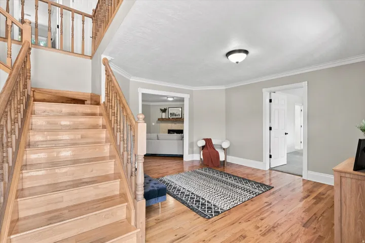 Hardwood flooring extending from the entryway to the staircase, white trim and crown molding, and a visible doorway leading to an additional area