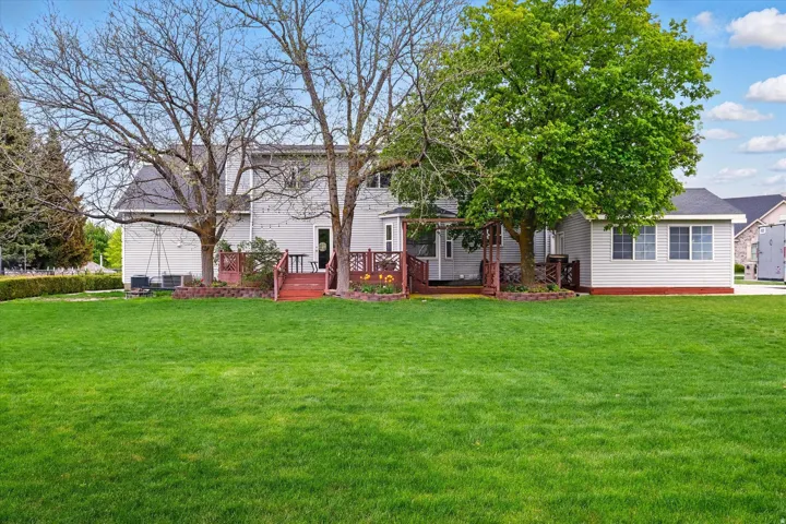 Expansive rear yard featuring a manicured lawn, mature trees, and a multi-level deck with red-stained railings