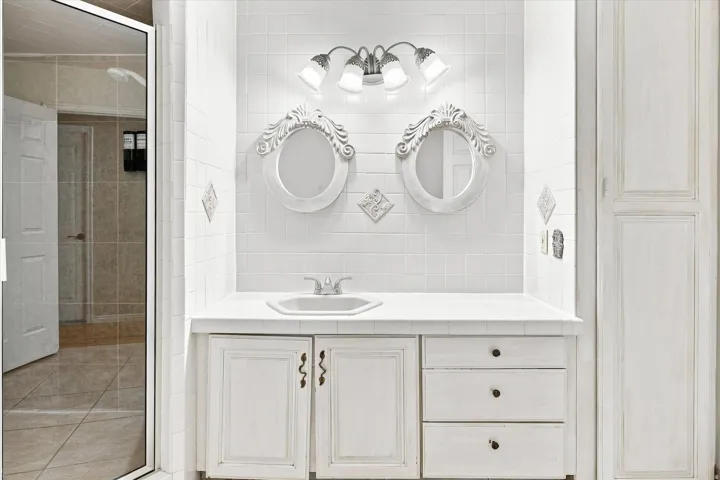 Bathroom vanity with an integrated sink, dual decorative mirrors, tile backsplash, and a three-light fixture
