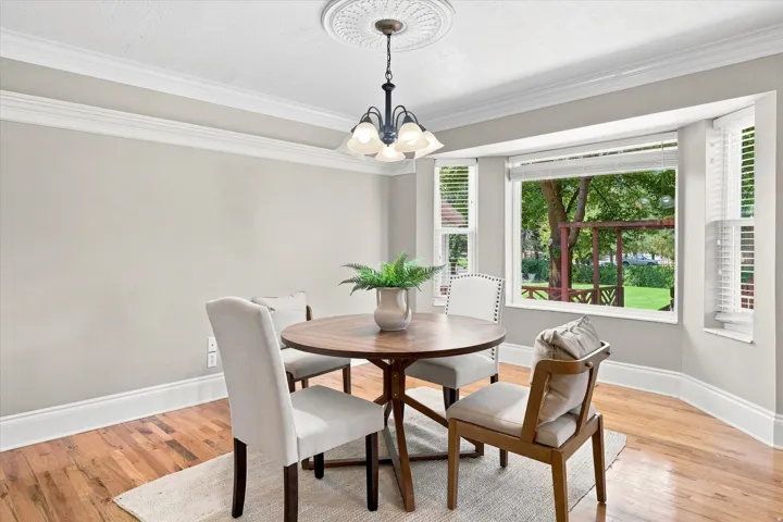 Dining area with a bay window, wood-finish flooring, white crown molding, and a ceiling medallion with a chandelier