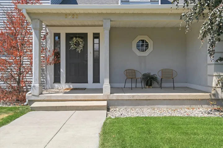 Covered front porch featuring a dark entry door with sidelights, an octagonal window, and concrete steps