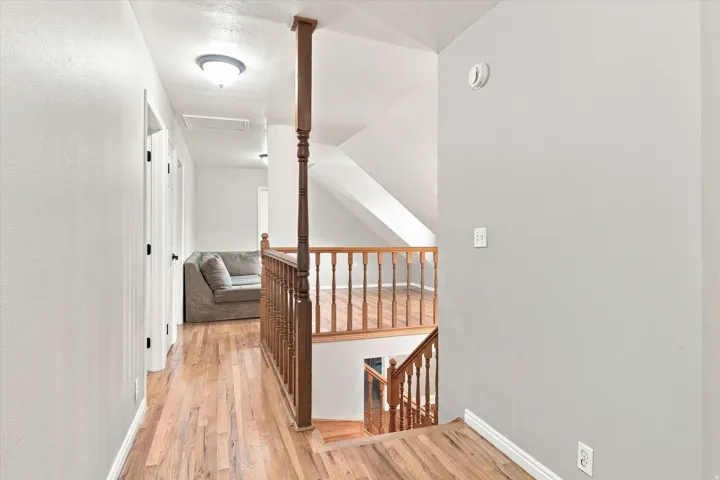 Upper-level hallway featuring wood-finish flooring, light-colored walls, and a wooden staircase with a matching railing