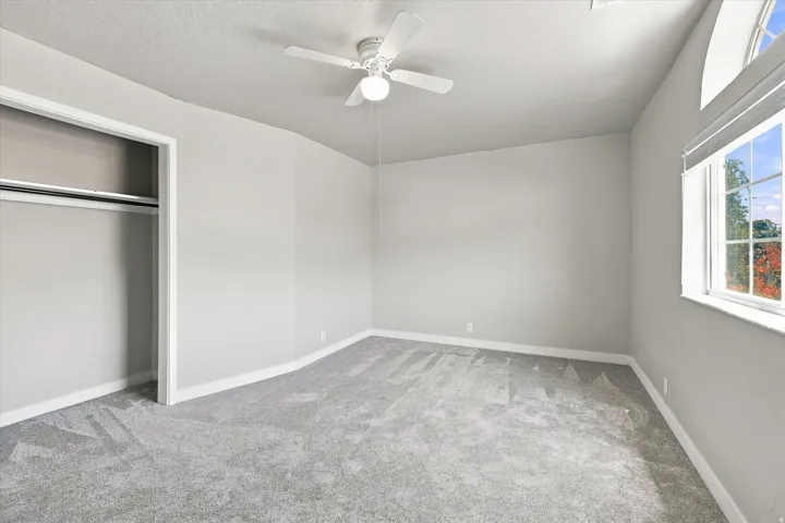 Carpeted interior space featuring a double-hung window with an arched transom, a ceiling fan, and an open closet