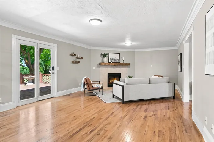 Spacious living area featuring wood-finish flooring, a corner fireplace with a mantel, and crown molding