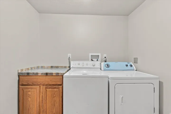 Laundry area featuring light-toned walls, wood-finish cabinetry, and a patterned countertop