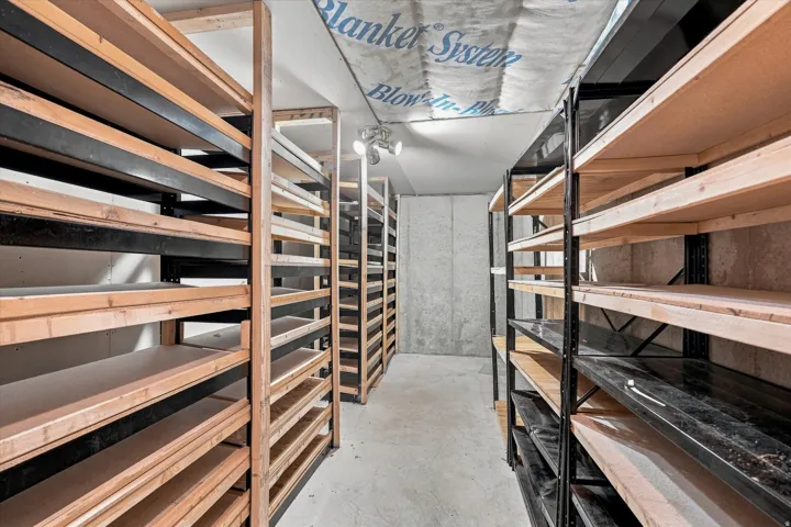 Dedicated storage room featuring extensive shelving units, concrete flooring, track lighting, and exposed ceiling insulation