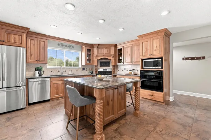 Spacious kitchen featuring warm wood cabinetry, stainless steel appliances, a large center island with a stone countertop, and tile flooring