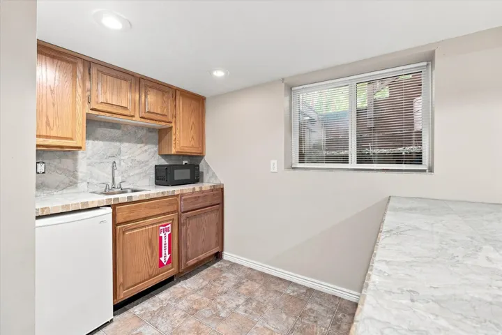 Compact kitchen area featuring wood-finish cabinetry, a single basin sink, and a tiled backsplash