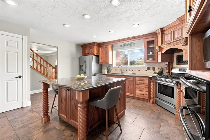 Kitchen featuring wood cabinetry, stainless steel appliances, granite countertops, and tile flooring